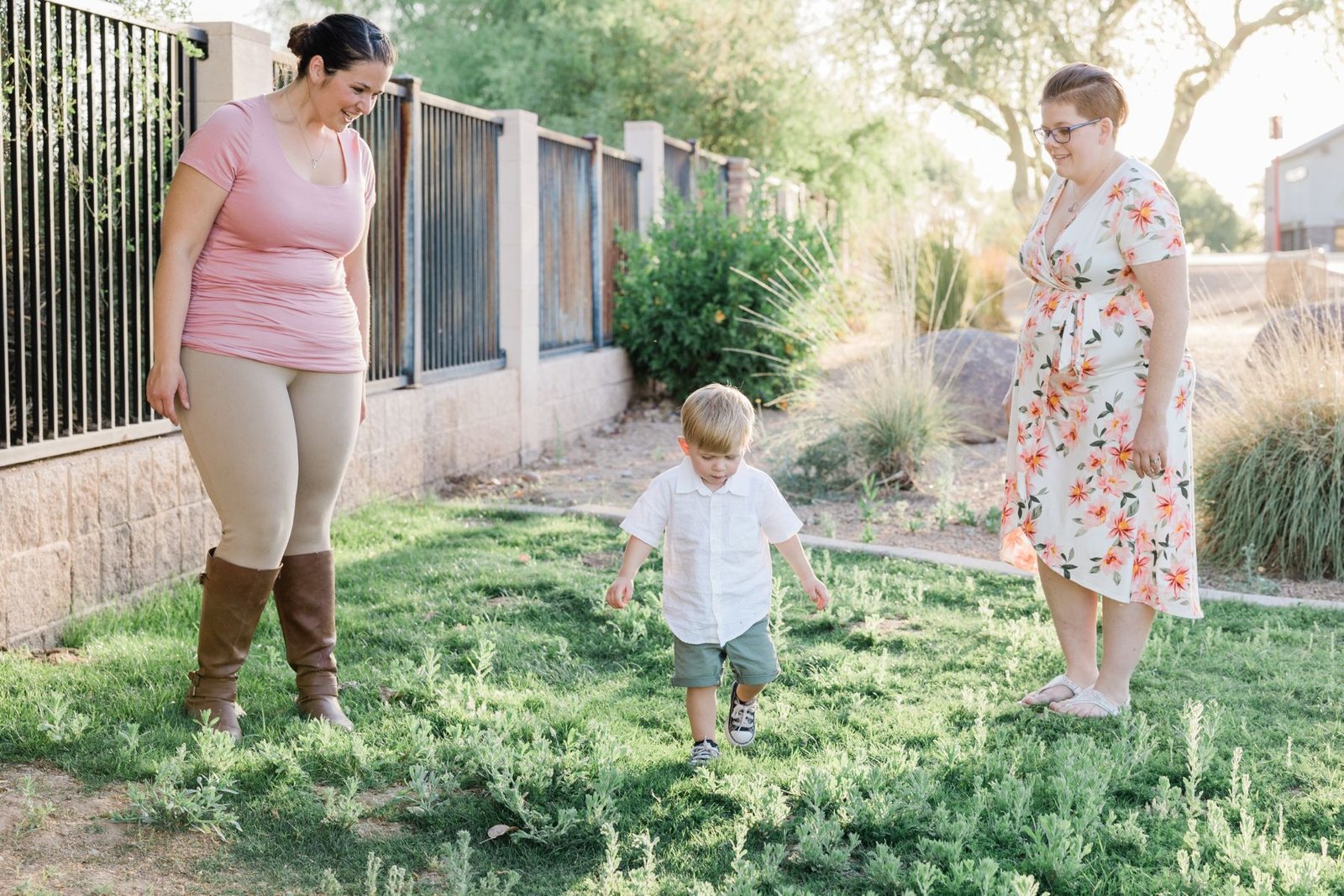 Two parents watching their toddler explore the yard